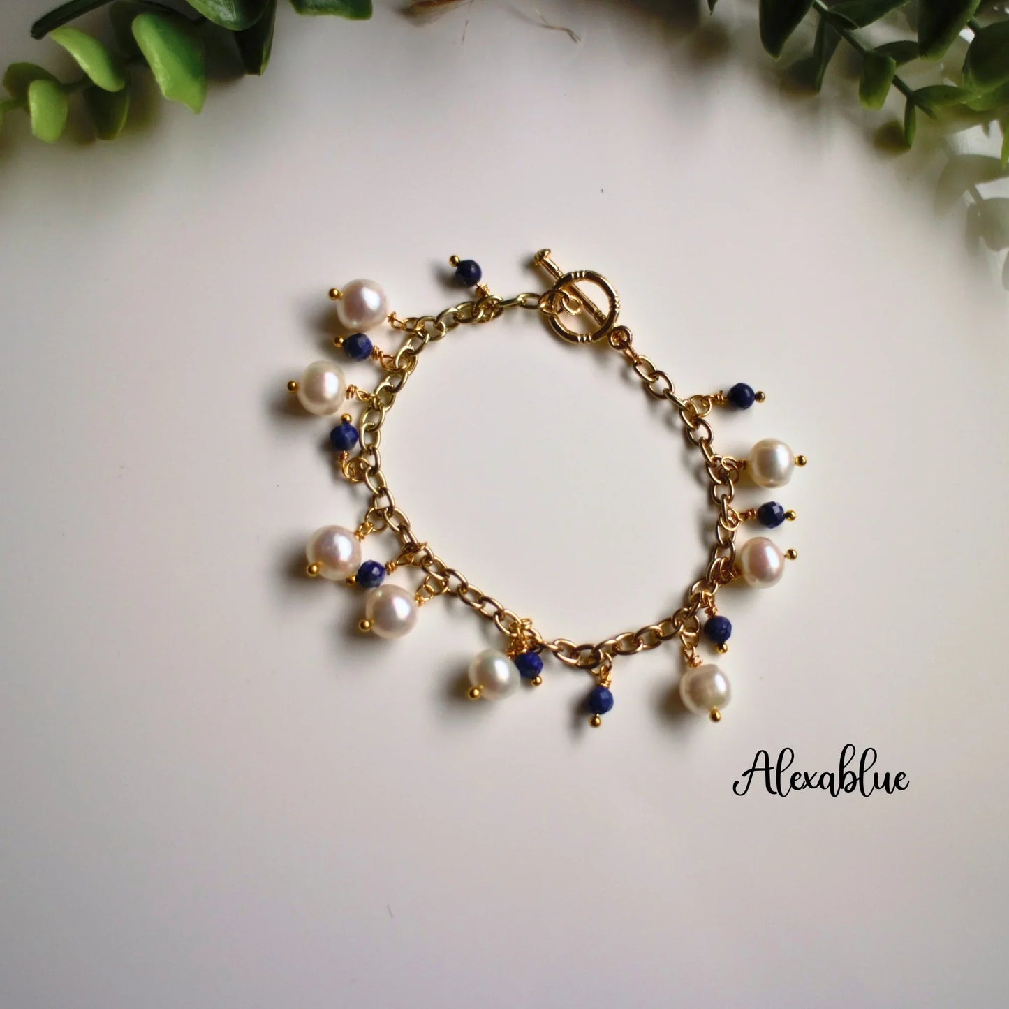 Gold chain bracelet with white pearls and blue gemstone charms on white background, natural lighting
