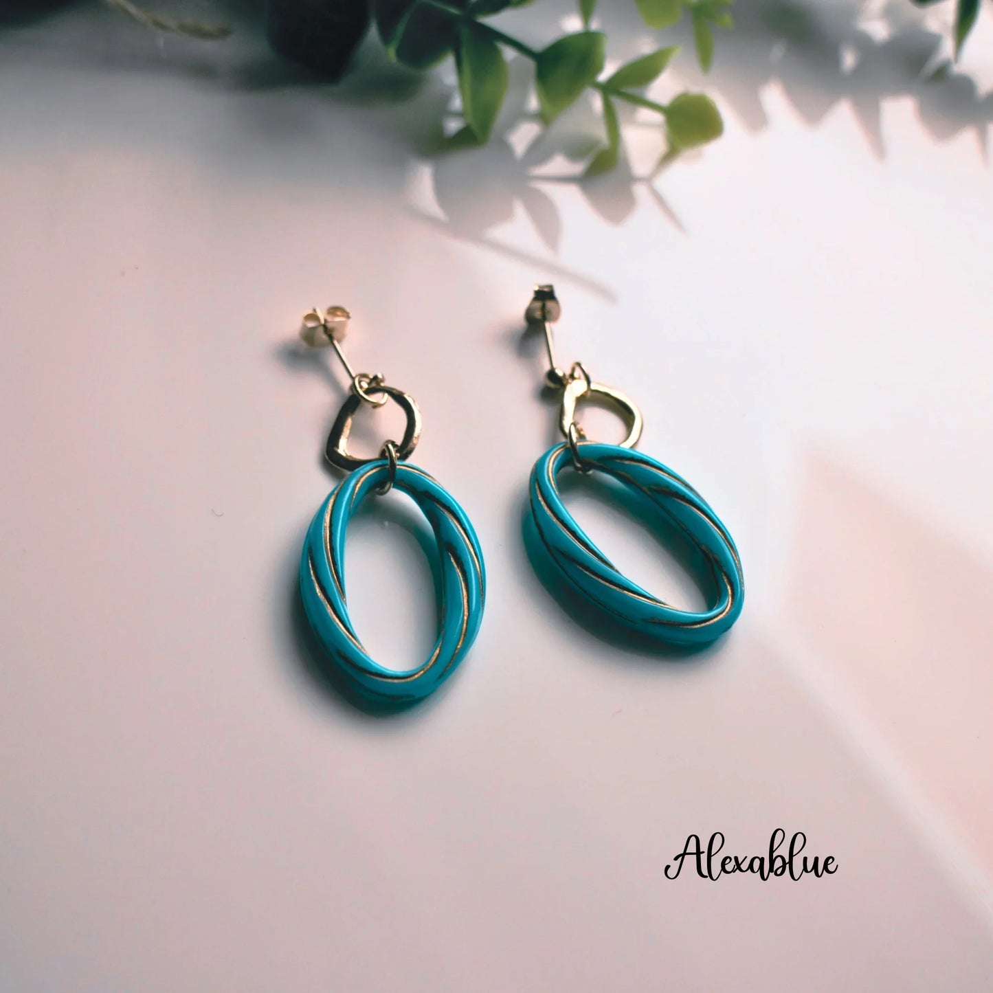 Turquoise natural stone oval drop earrings with gold accents on white background, decorative greenery
