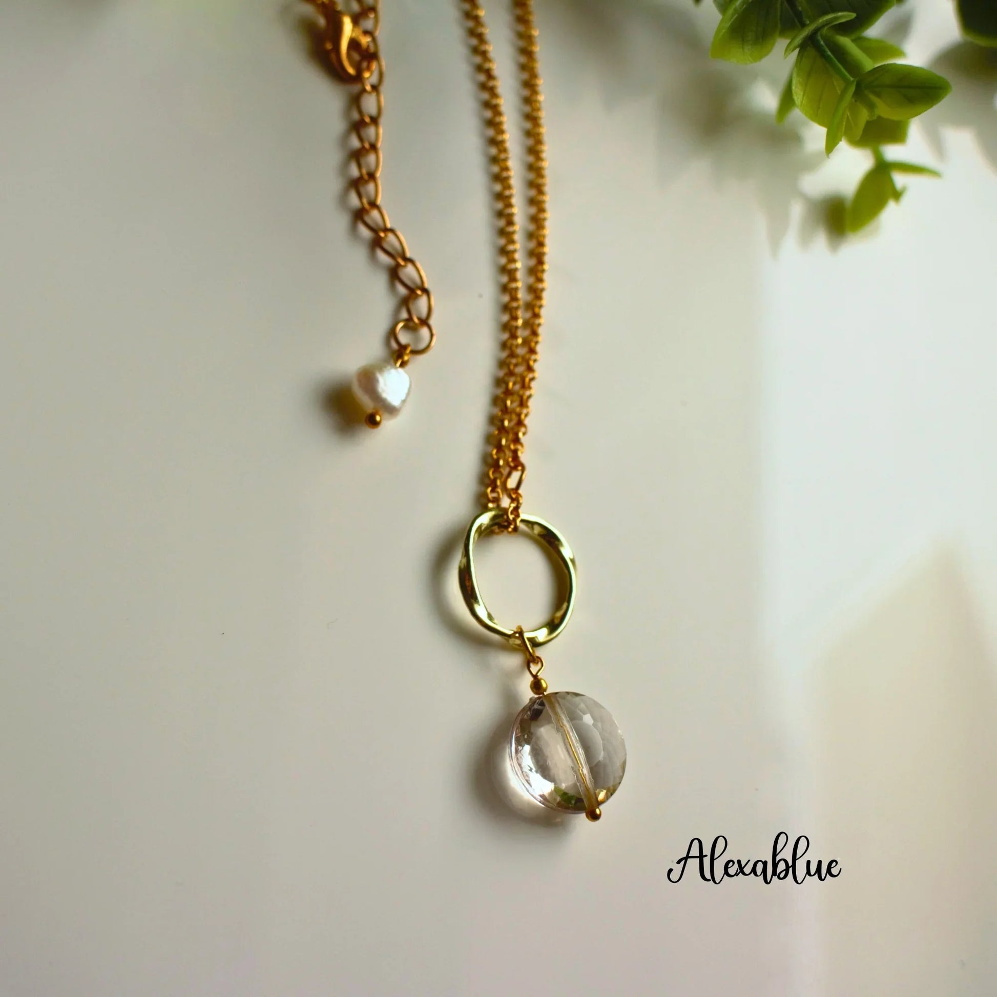 Gold chain necklace with clear round gemstone pendant and pearl accent on white surface
