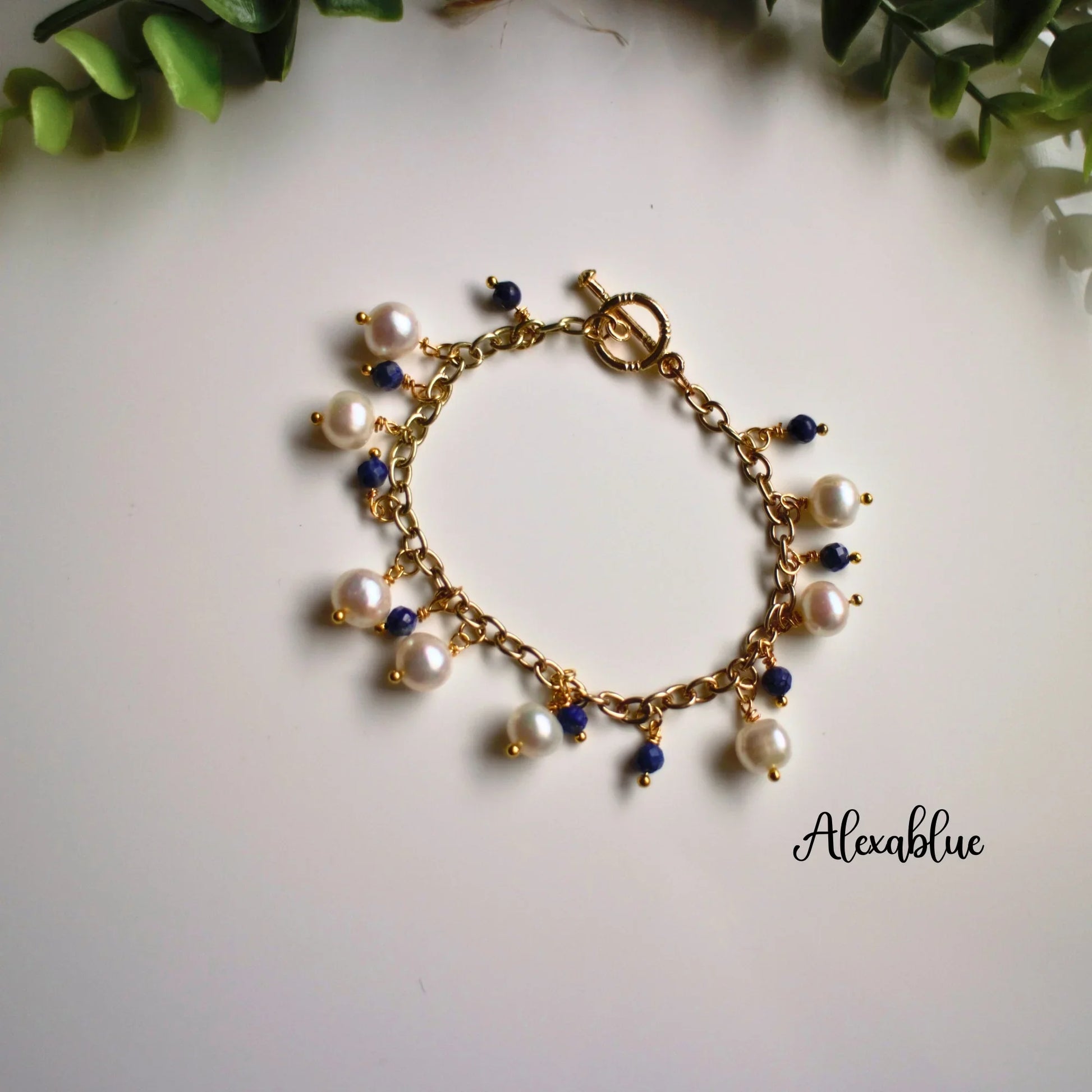 Gold chain bracelet with white pearls and blue gemstone charms on white background, natural lighting