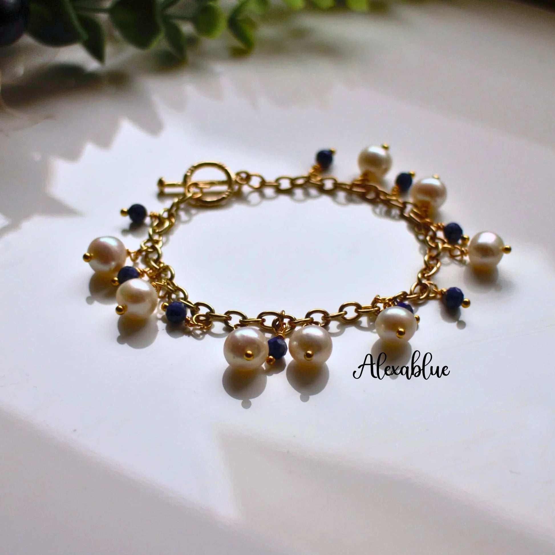Gold chain bracelet with natural pearls and blue stone beads on a white surface