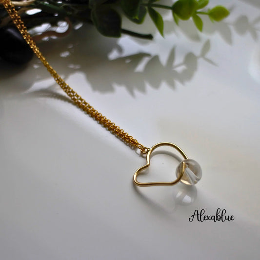 Gold chain necklace with heart-shaped pendant and clear natural stone, displayed on white surface.