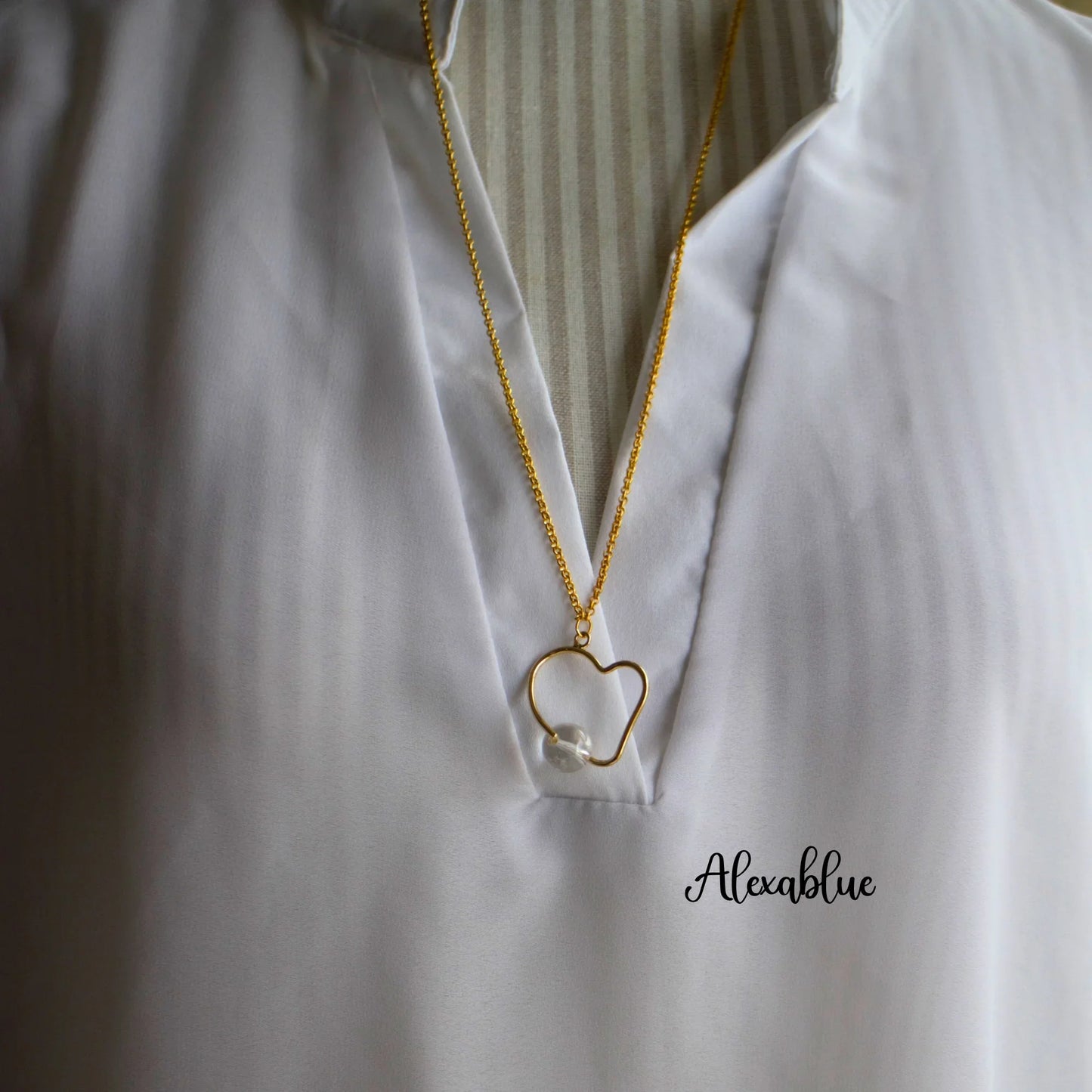 Gold heart pendant necklace with pearl accent on white blouse