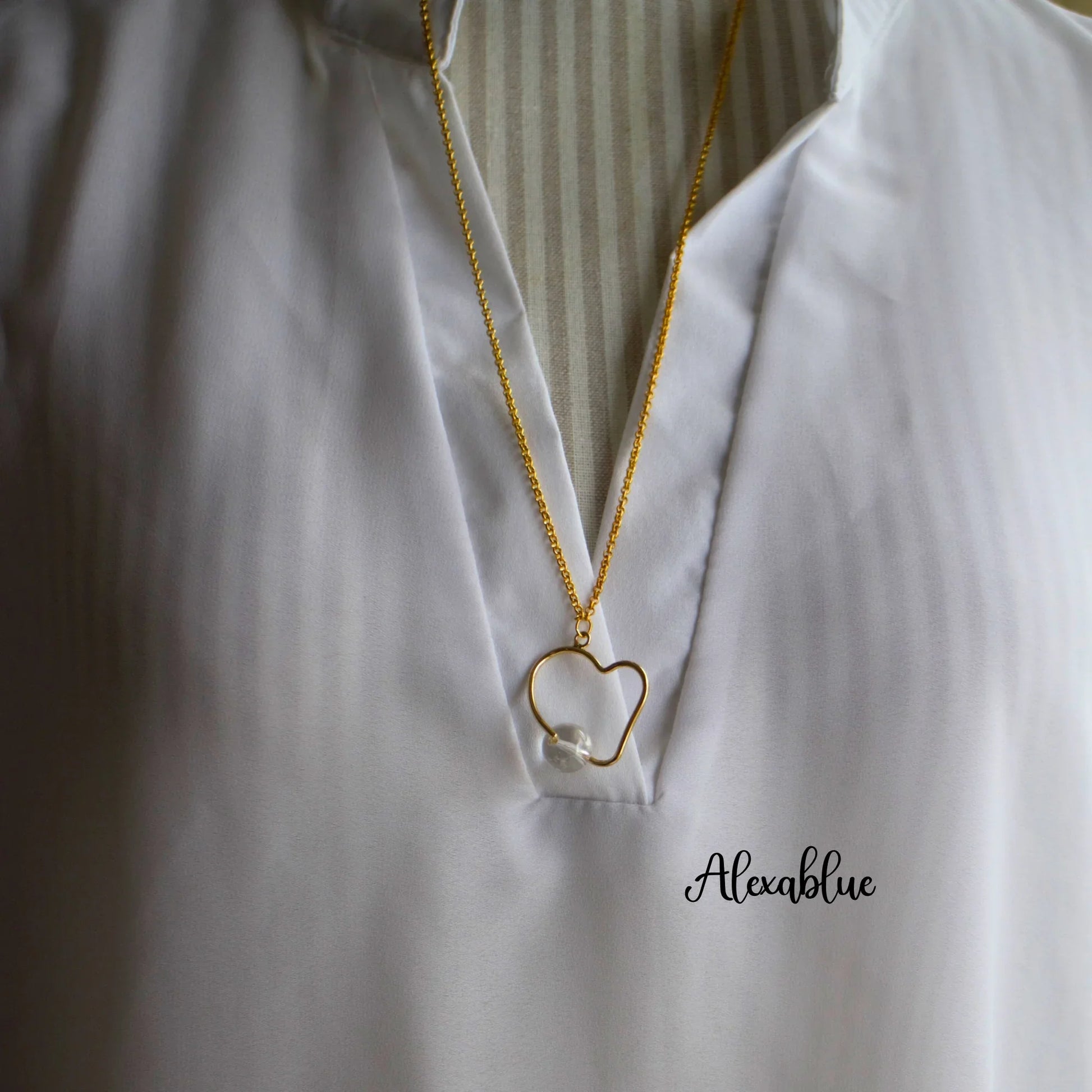 Gold heart pendant necklace with pearl accent on white blouse