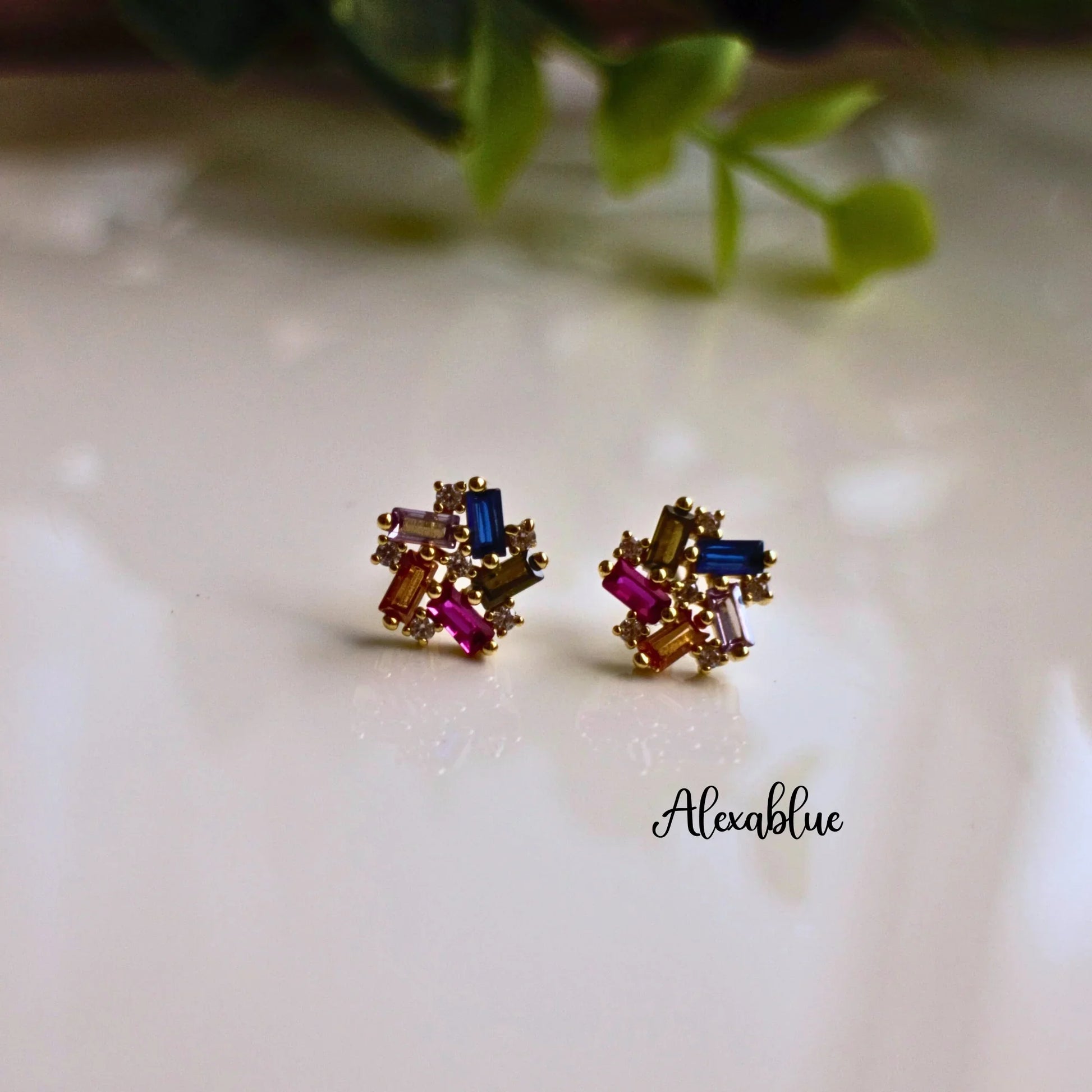 Gold stud earrings with multicolored rectangular gemstones on a glossy surface