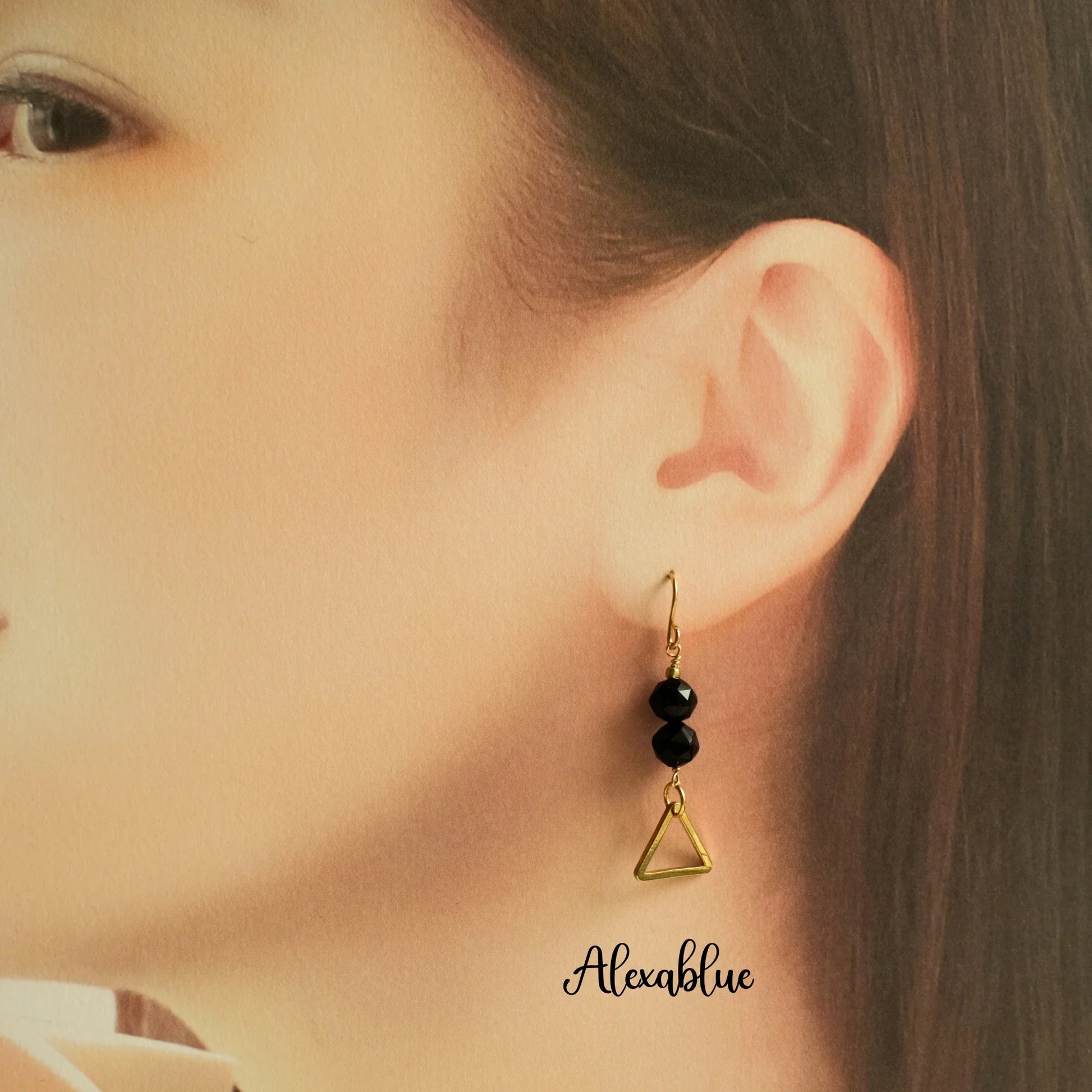 Gold triangle drop earring with black natural stone beads worn on a woman's ear