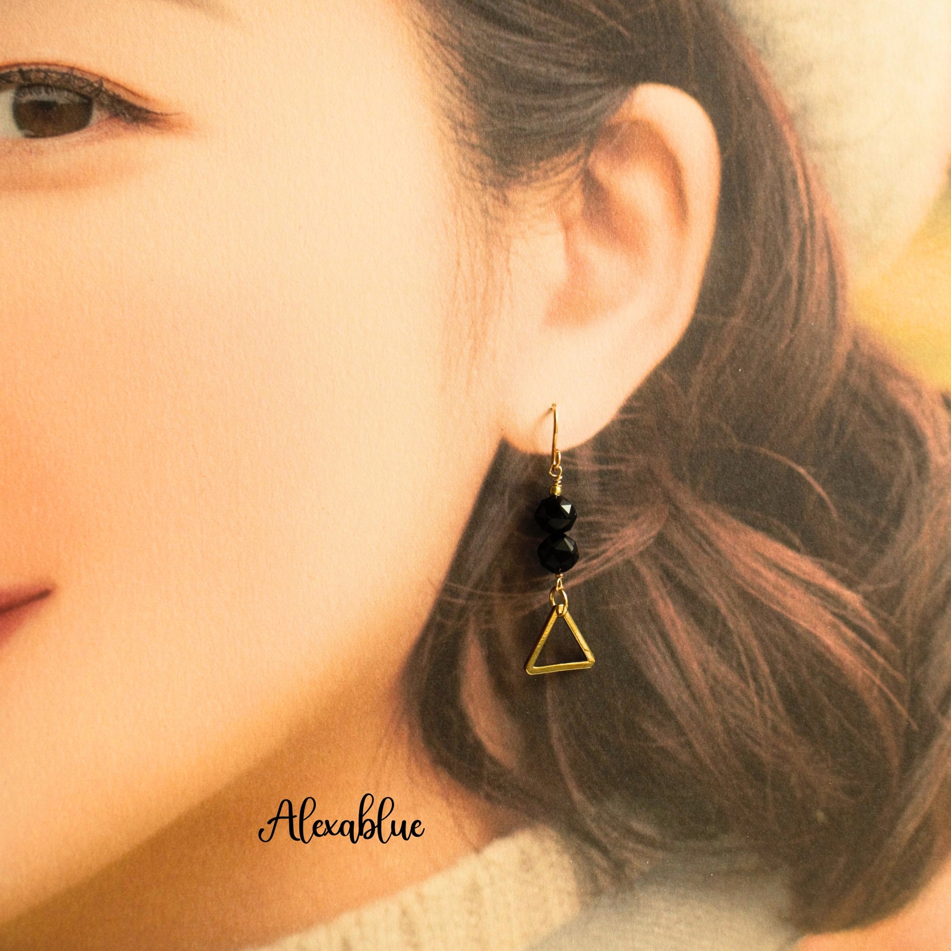 Gold dangle earring with black natural stone beads and triangle charm on woman's ear