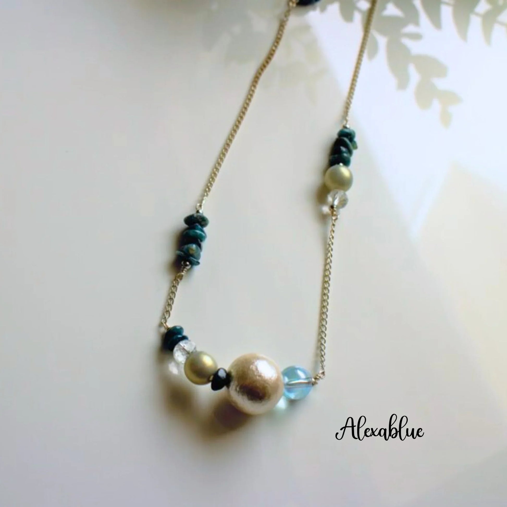 Gold chain necklace with natural stones, pearls, and crystal beads on a white background.