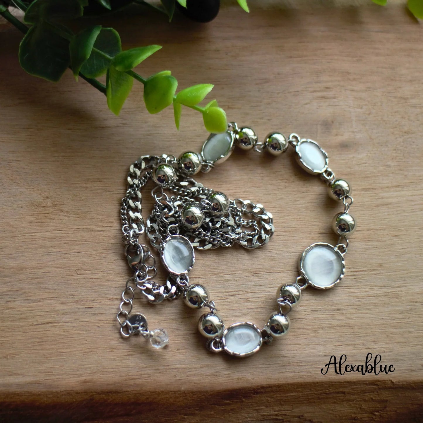 Silver chain necklace with round natural stone accents on wooden surface, green plant decor