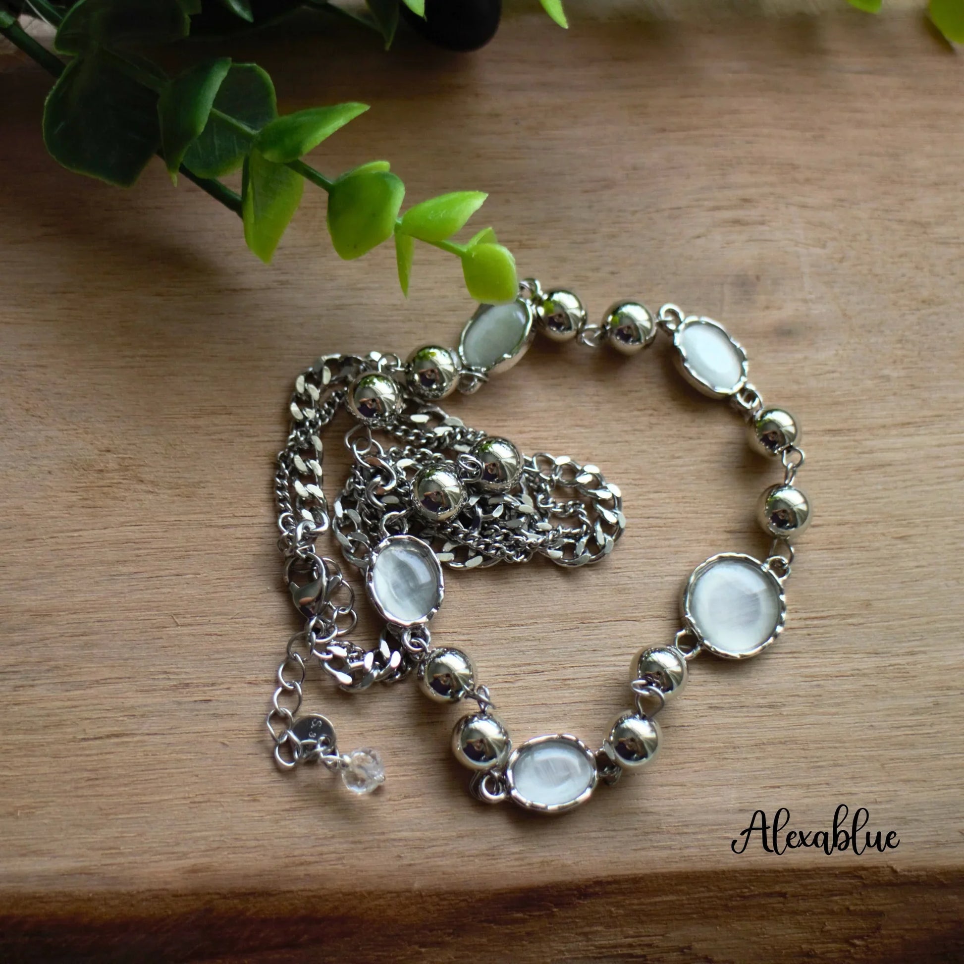 Silver chain necklace with round natural stone accents on wooden surface, green plant decor