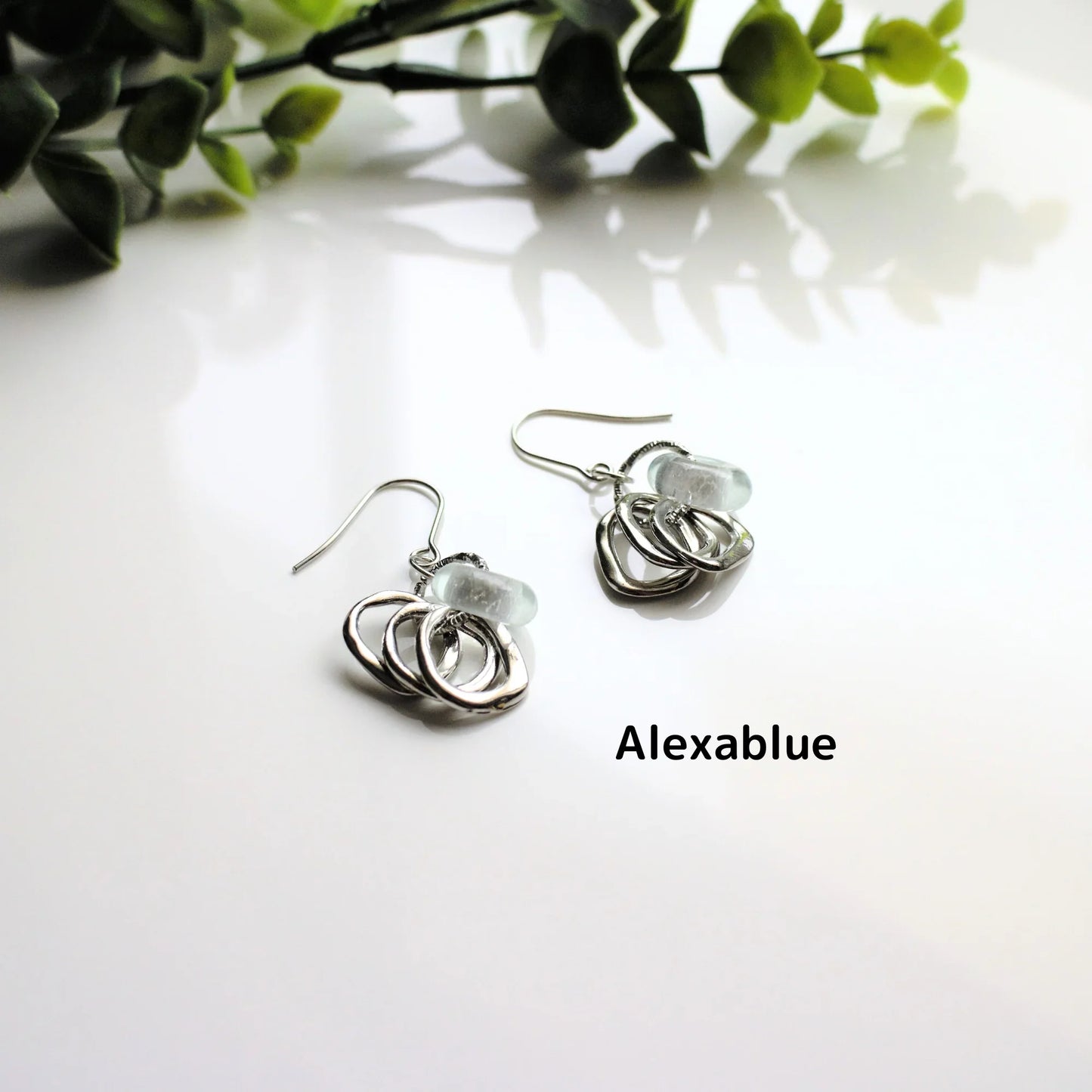 Silver natural stone drop earrings with textured hoops on white surface, greenery background