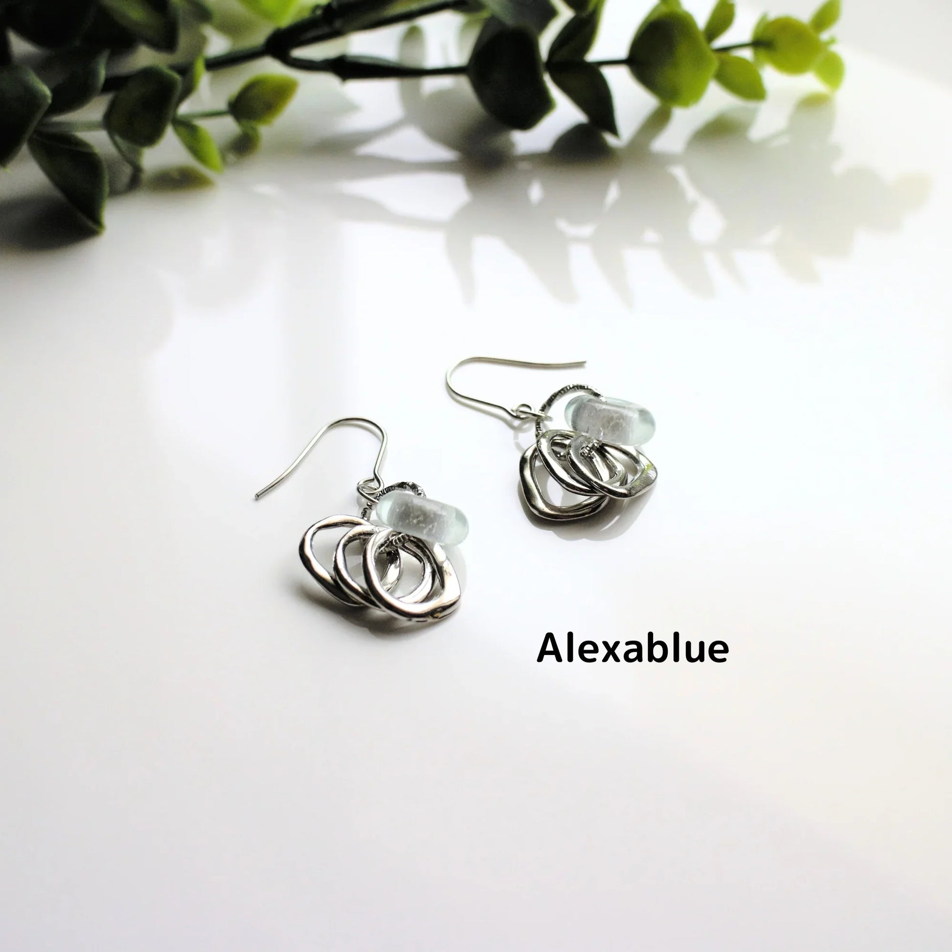 Silver natural stone drop earrings with textured hoops on white surface, greenery background