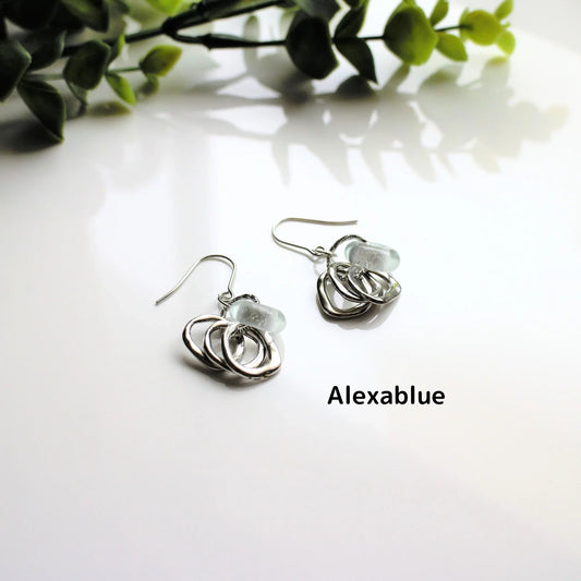 Silver natural stone drop earrings with textured hoops on white surface, greenery background