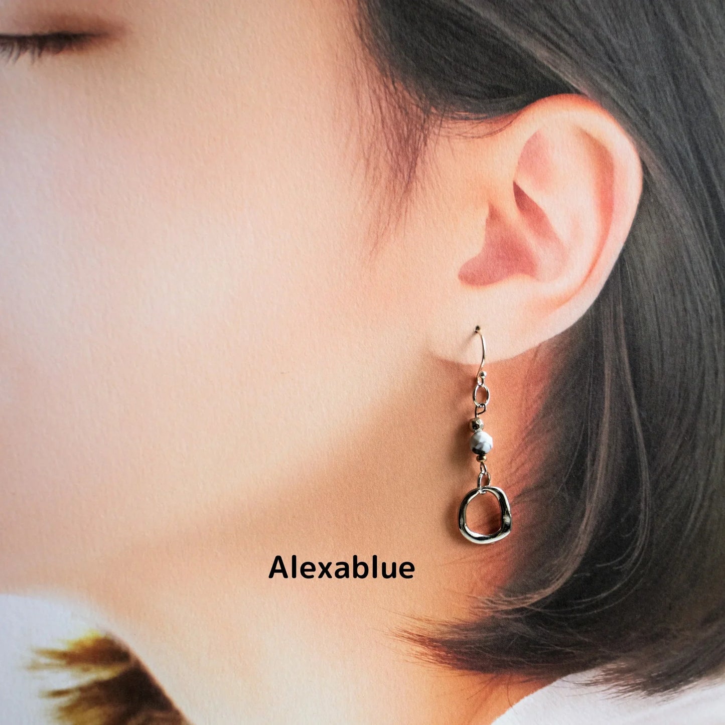 Woman wearing natural stone dangle earring with round metal detail, close-up view