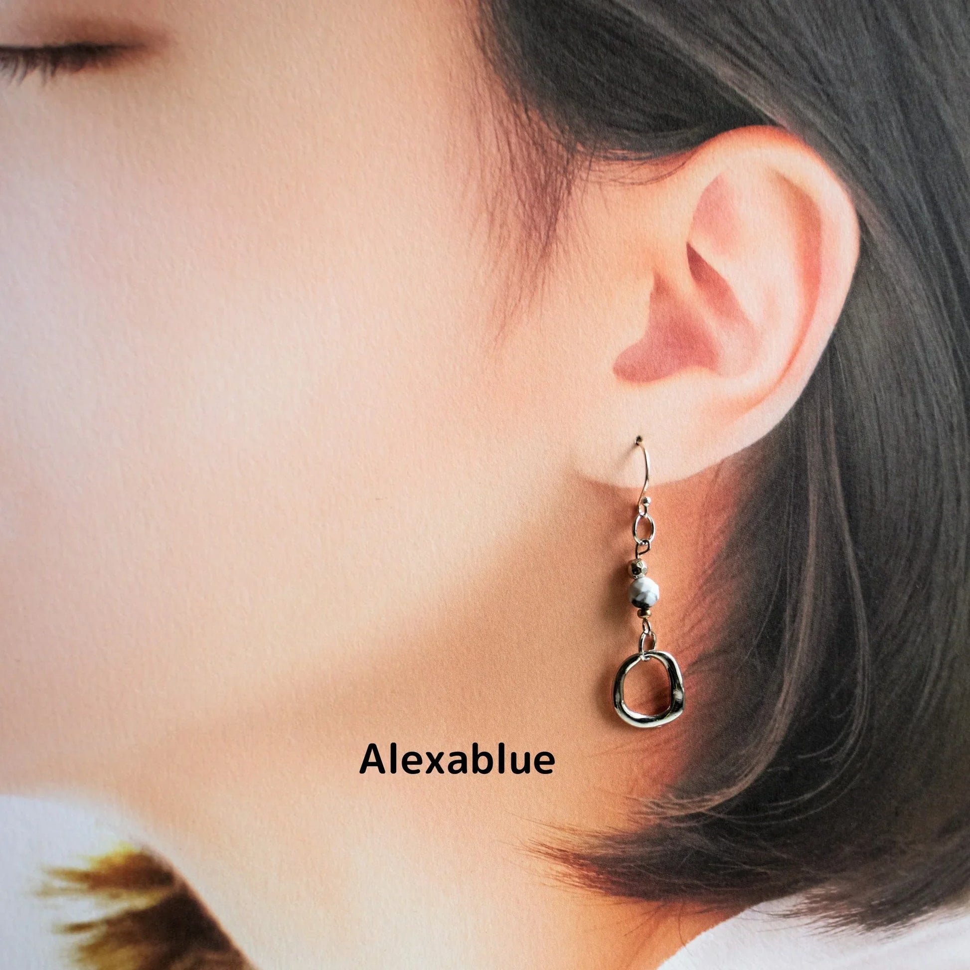 Woman wearing natural stone dangle earring with round metal detail, close-up view