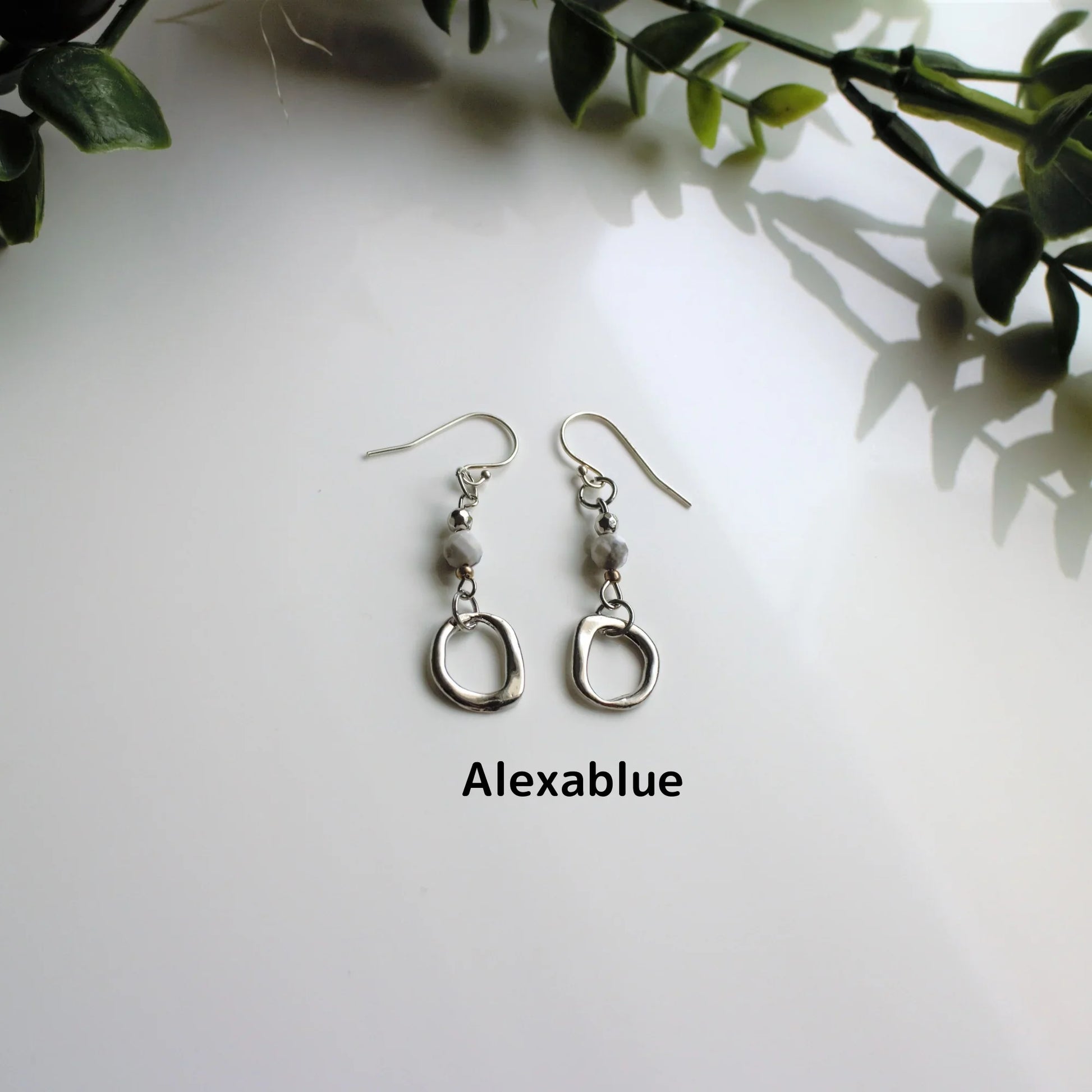Silver dangle earrings with round natural stones on white background, greenery decor
