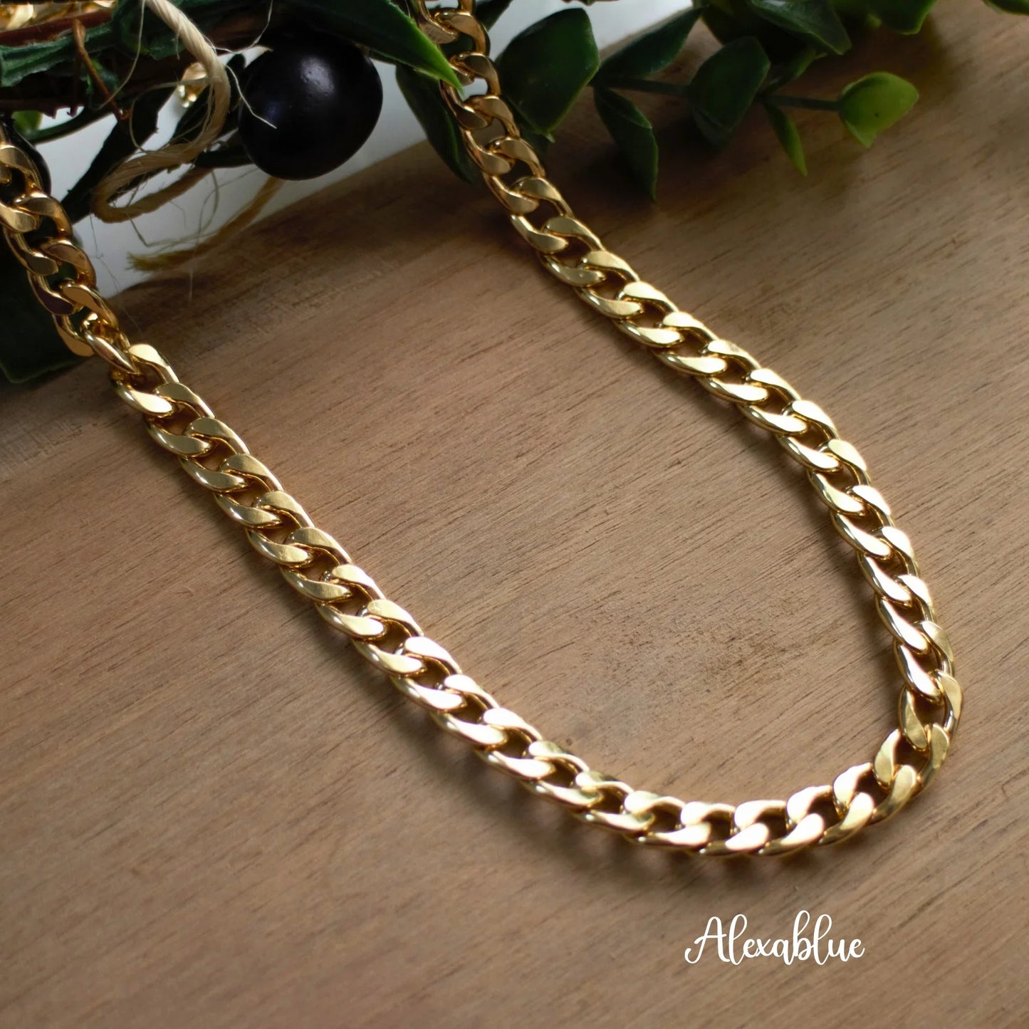 Gold chain necklace with curb links on wooden surface, natural stone jewelry style