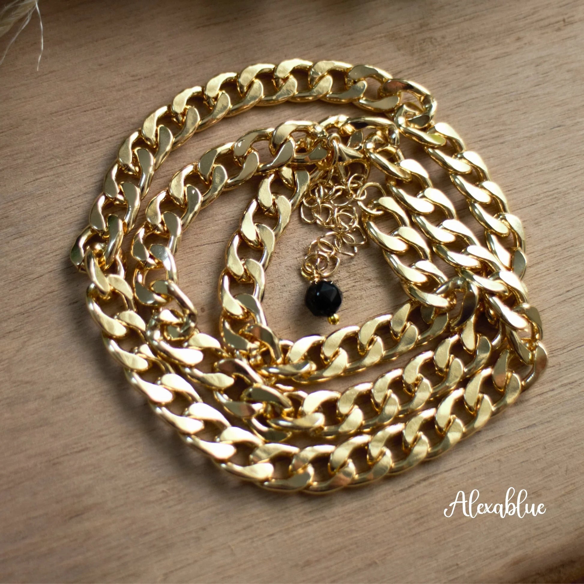 Gold chain necklace with black stone accent on wooden surface, luxury jewelry accessory