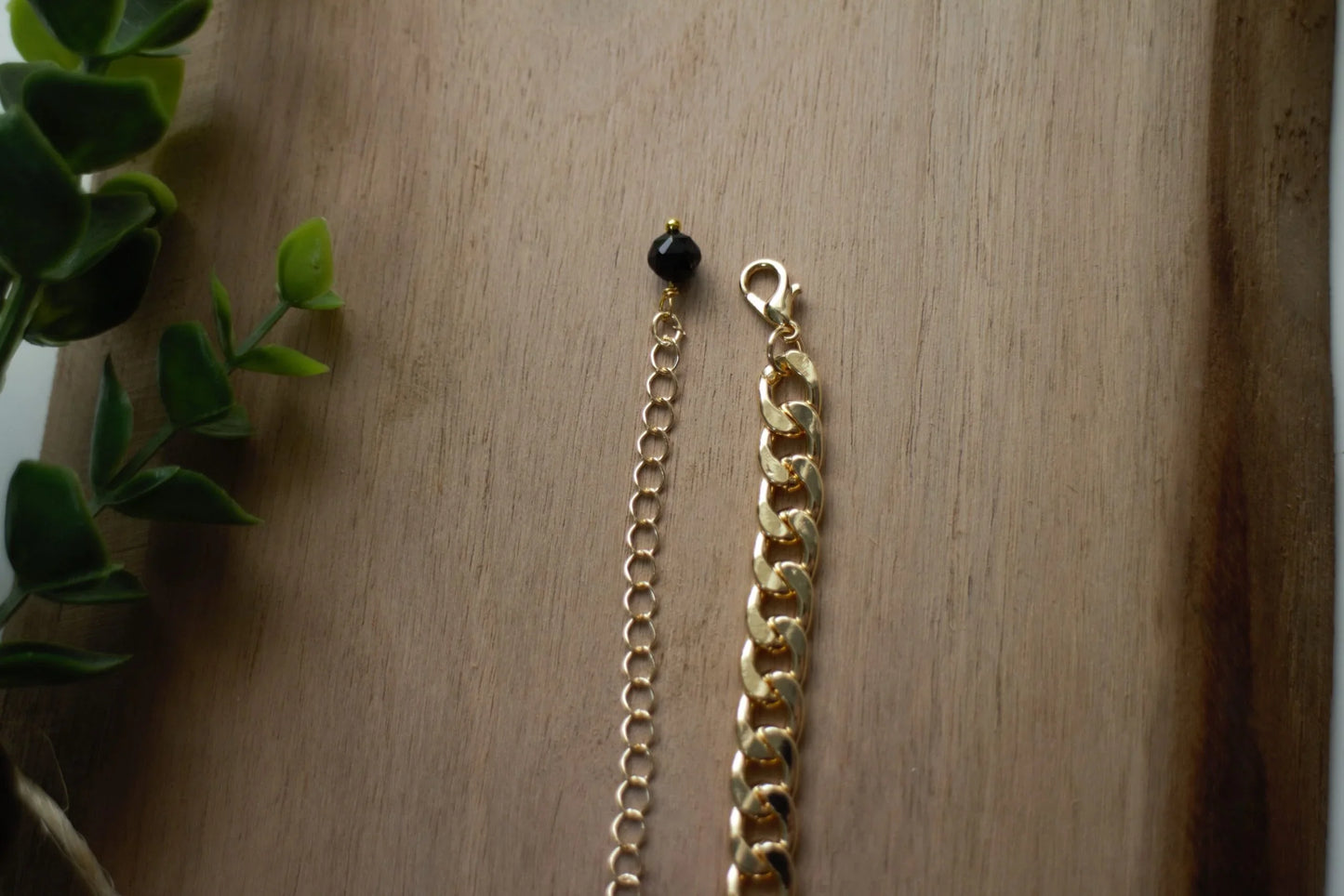 Gold chain bracelet with black stone accent on wooden surface, natural stone jewelry