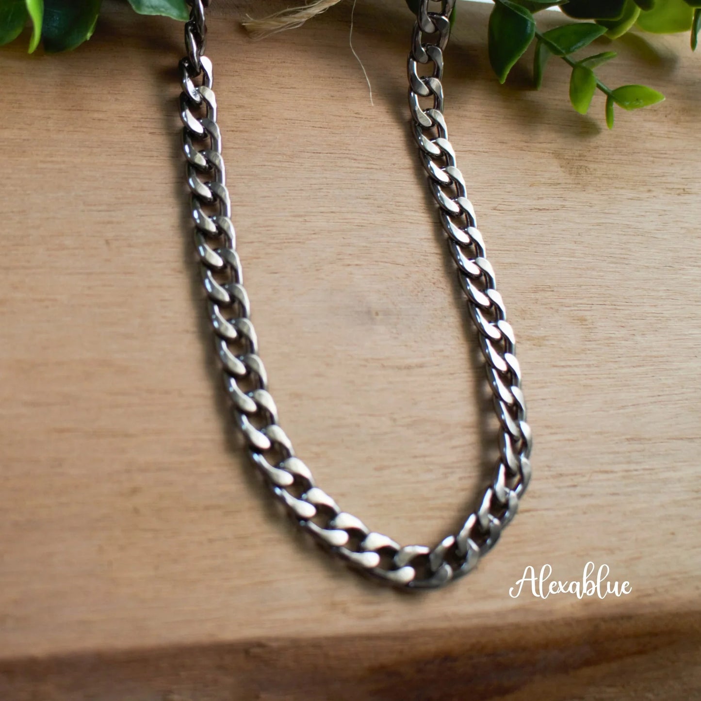 Chunky silver chain necklace on wood surface with green leaves, men's jewelry accessory.