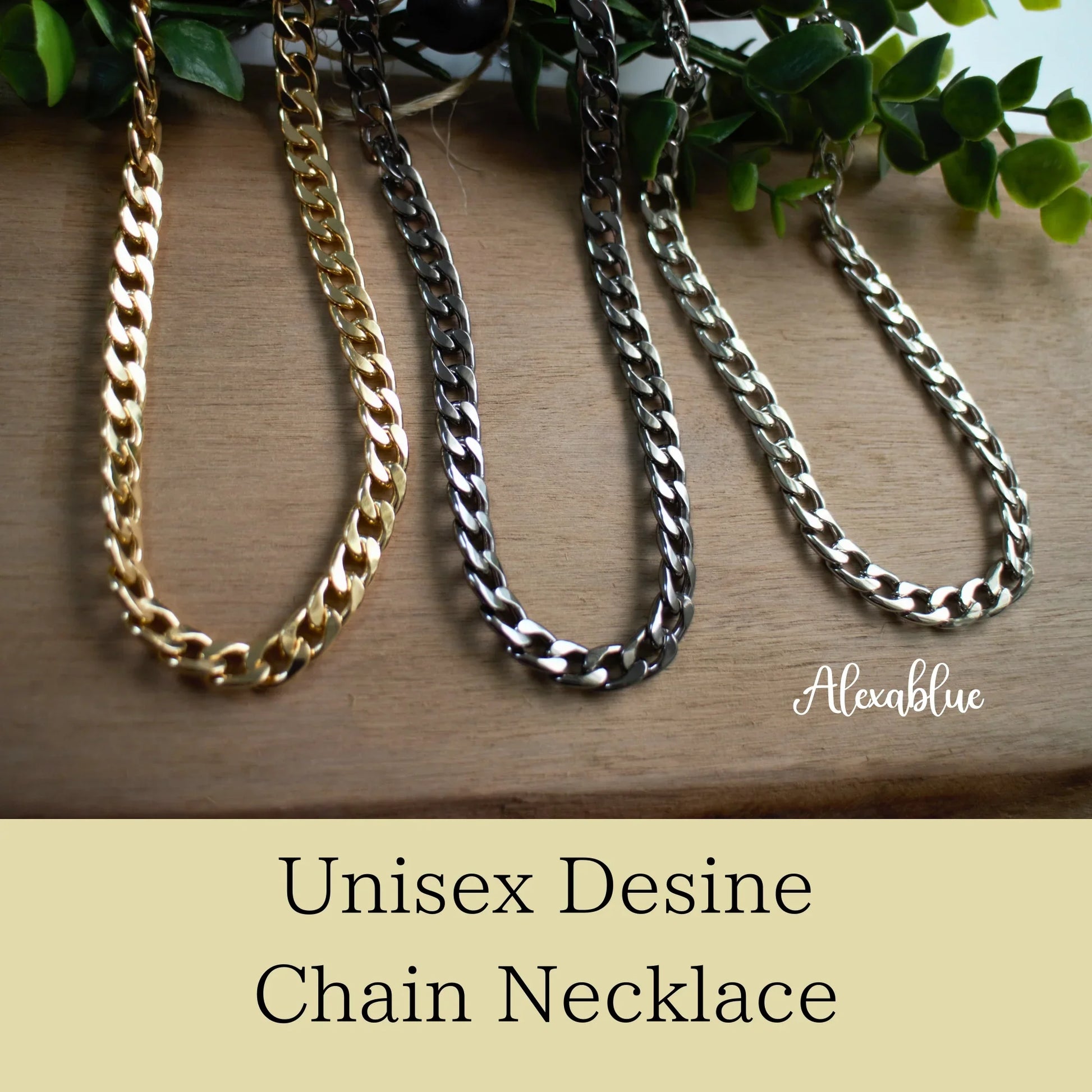 Three unisex curb chain necklaces in gold, black, and silver on wooden surface with greenery.