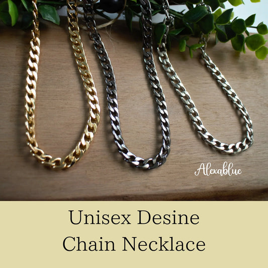 Three unisex curb chain necklaces in gold, black, and silver on wooden surface with greenery.