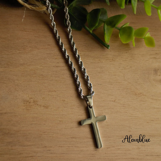 Silver rope chain cross necklace on wooden surface with green leaf decor