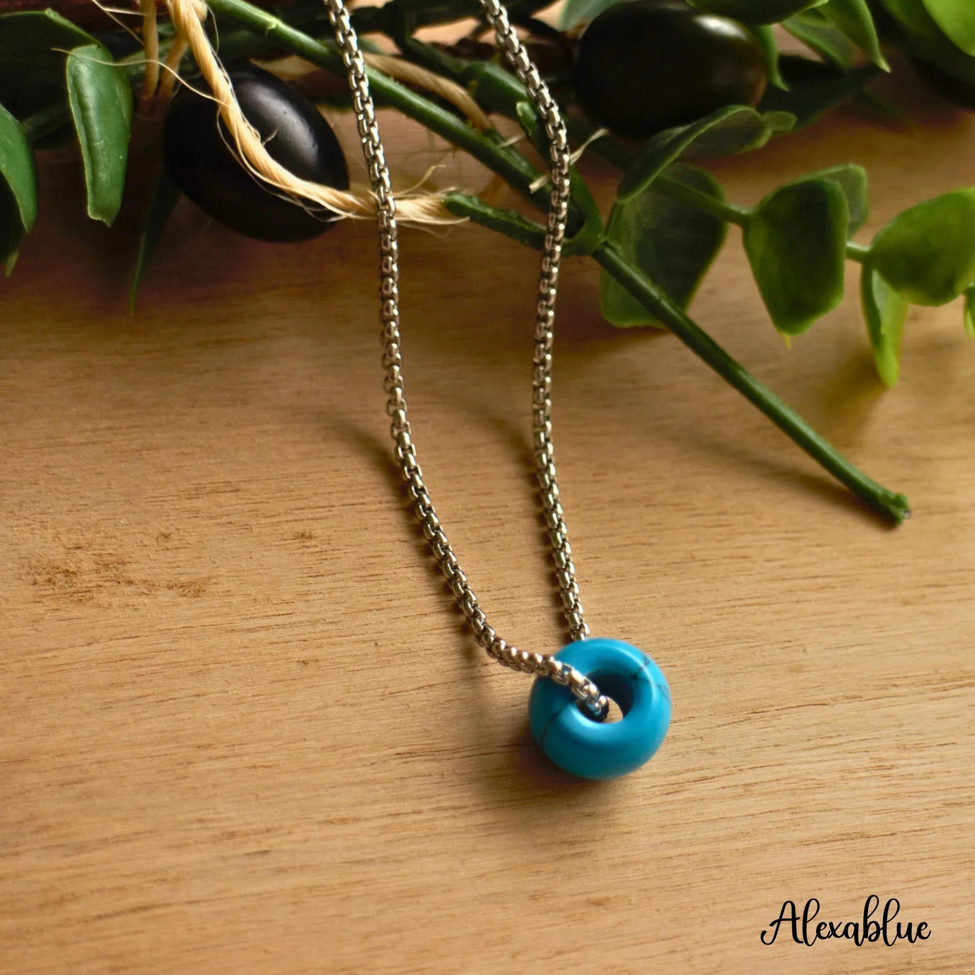 Turquoise stone pendant necklace with silver chain on wooden surface, greenery background