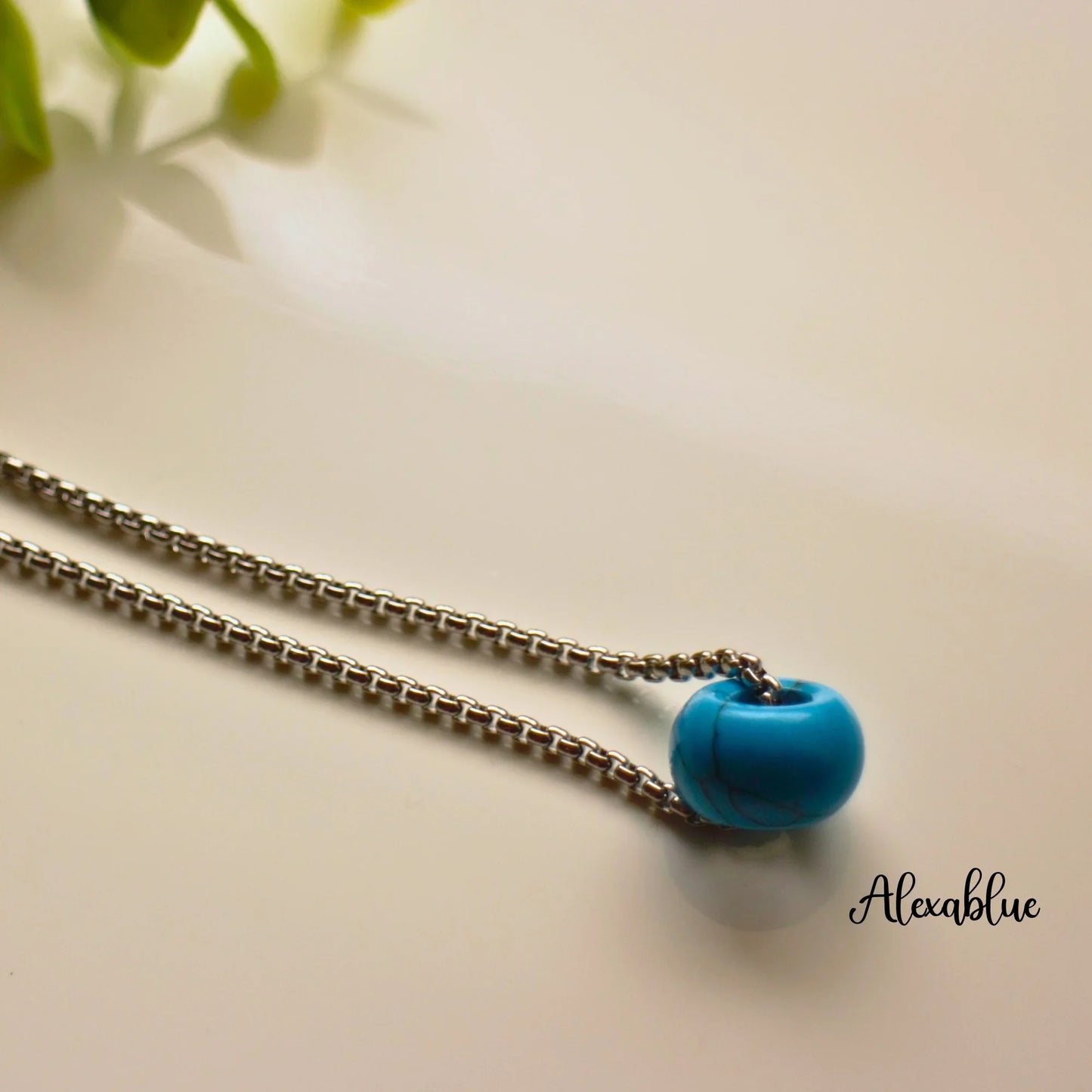 Silver chain necklace with turquoise round natural stone pendant on a white background.