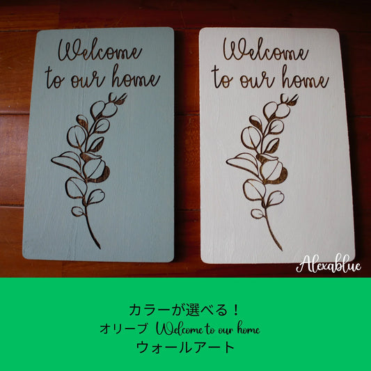 Two wooden wall art plaques with olive branch design and 'Welcome to our home' text, in blue and white color options.